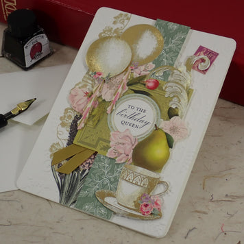 A handcrafted birthday greeting card with vintage-style collage elements including balloons, flowers, a teacup, and a central oval label reading 'to the birthday queen.' 