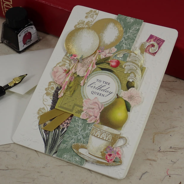 A handcrafted birthday greeting card with vintage-style collage elements including balloons, flowers, a teacup, and a central oval label reading 'to the birthday queen.' 