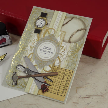 A baseball-themed handcrafted Birthday greeting card with gold foil details, a baseball graphic, a watch, and sports tools, styled on a desk next to a red book, fountain pen, and ink bottle.