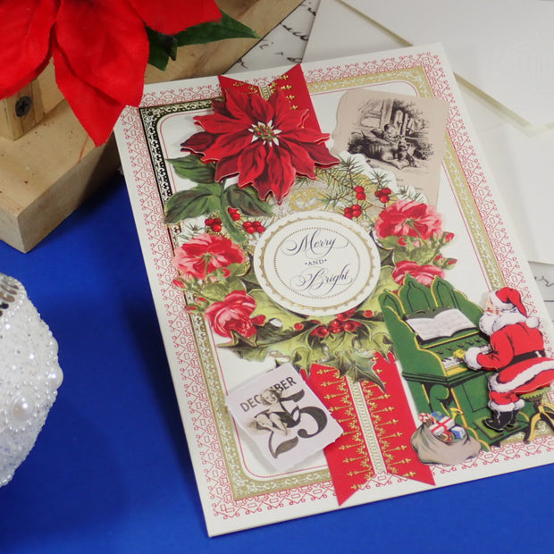 A handcrafted Christmas greeting card with red poinsettias, a Santa figure, and a central round label reading 'Merry and Bright,' styled on a blue surface with holiday props.