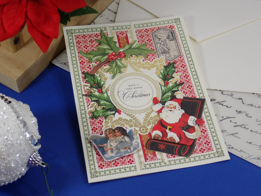 A handcrafted Christmas greeting card with a vintage Santa Claus illustration, holly, red patterned background, and a central oval reading 'Merry Christmas.'