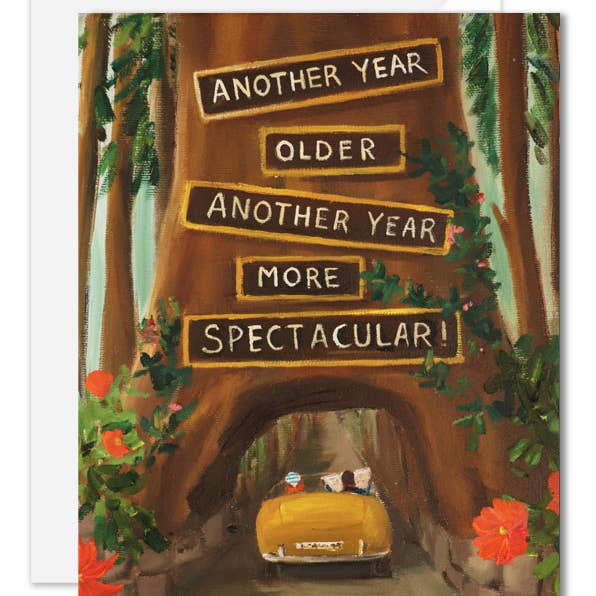A rectangle birthday greeting card that is artisan made. Featuring a painted forest scene with a yellow convertible driving through a tree arch. Large tilted text boxes read, 'ANOTHER YEAR OLDER ANOTHER YEAR MORE SPECTACULAR!'.