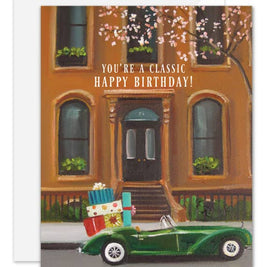 Artisan made, Birthday greeting card with a green car carrying presents in front of a brownstone building.